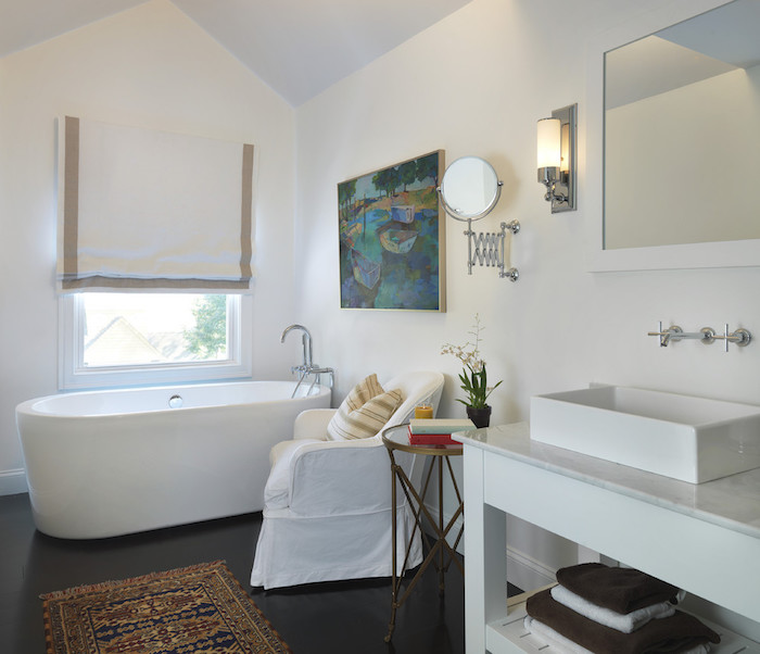 murs blancs avec tableau d art sur mur blanc, baignoire blanche sur sol gris foncé, miroir salle de bain, meuble blanc avec vasque, tapis oriental