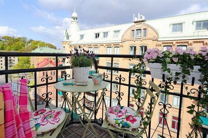 idée aménagement petit balcon fleuri avec des bacs et pots de fleur, chaises métalliques décorées de coussins à motifs fleuris