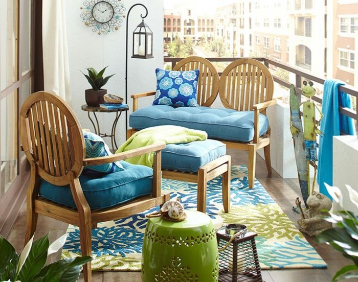 chaise et canapé en bois avec des coussins d assise bleus, tapis à motifs fleuris, revetement carrelage aspect bois, ambiance exotique amenagement balcon
