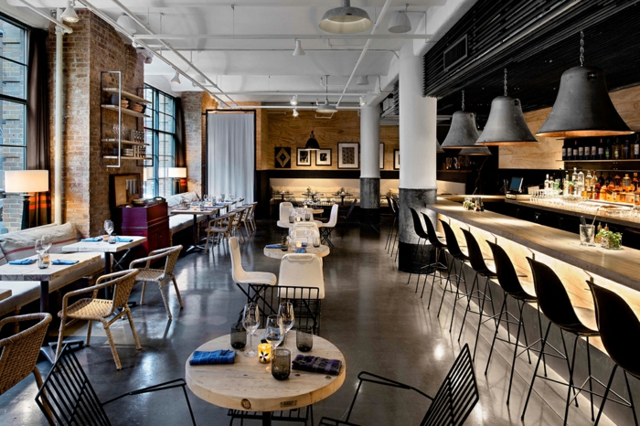 joli café en style loft industriel, lampes suspendues, petites tables carrées, plafond blanc, chaises de bar noires
