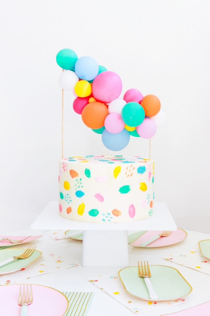 gateau anniversaire dessin aquarelle réalisé avec du glaçage coloré, orné d'un cake topper de mini-ballons 