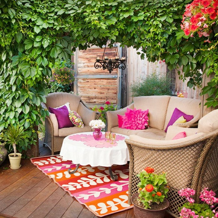 exemple de decoration balcon fleuri avec canapé et fauteuils marron, table basse décorée à motifs fleuris, tapis multicolore, arche de végétation verte