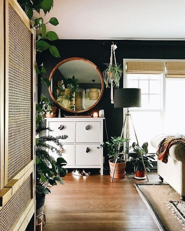 Intérieur moderne dans une pièce avec beaucoup de plantes vertes, miroir ronde, lampe à trois pieds, canapé beige, tapis persienne, salle de sejour murs bleu fonce
