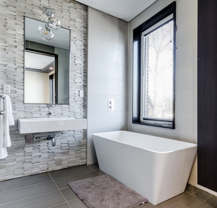 une ambiance relaxante dans une salle de bains qui combine trois types de carreaux dans les tons gris, carrelage en mosaïque posé en crédence derrière le plan vasque