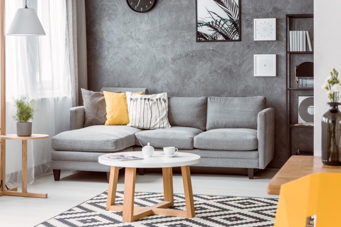 aménagement salon minimaliste aux murs à texture béton avec meubles bois et canapé d'angle gris, modèle tapis scandinave blanc et noir