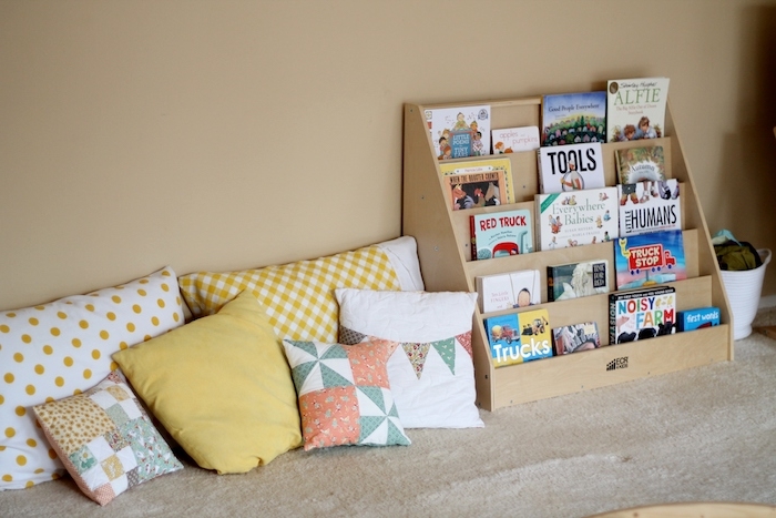 coin lecture avec multitude e coussins contre un mur, étagère en bois avec des livres rangés, murs beige