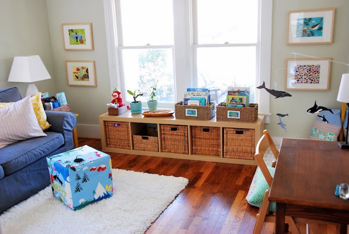 etagere basse bois avec rangement en paniers à jouets, parquet marron, tapis blanc, canapé bleu, matelas d activité au sol, coin montessori dans le salon