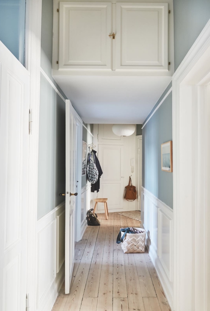 un couloir long et étroit de style scandinave avec un soubassement en moulure murale blanche et des murs peints en bleu gris clair