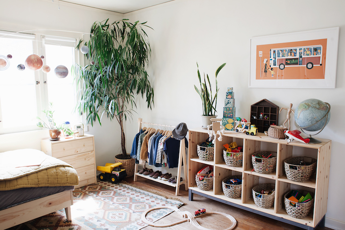 etagere meuble rangement jouet en bois avec paniers pour ranger les jouets, murs blancs, grande plante verte, tapis coloré, lit en bois, dressing enfant ouvert