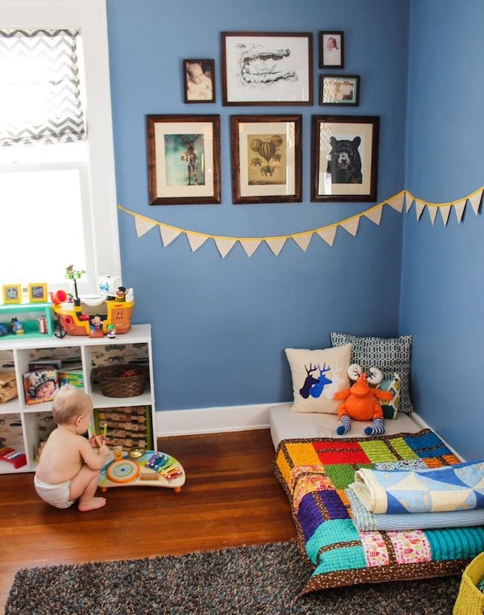 deco chambre bebe garcon en bleu avec ambiance montessori, murs bleu foncé, matelas au sol avec couverture colorée, meuble rangement jouet bas, mur décoré de cadres