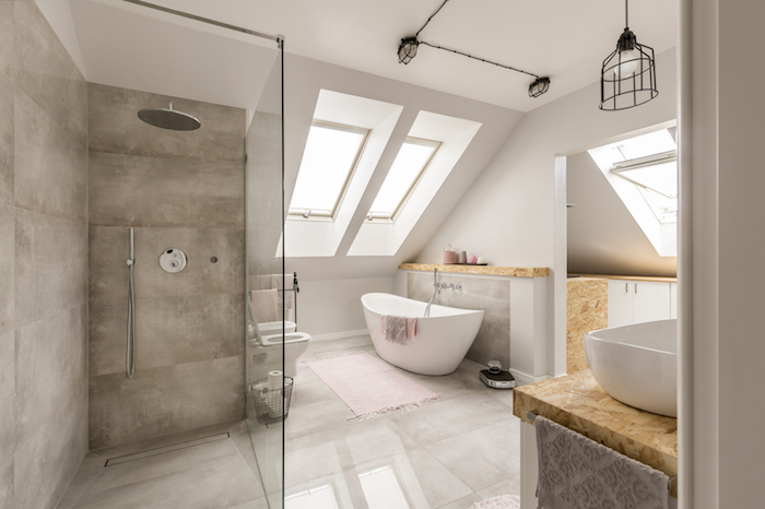 modele de salle de bain mansardée avec carrelage gris, paroi verre, baignoire blanche, tapis rose, fenêtres de toit, meuble salle de bain bois avec vasques à poser