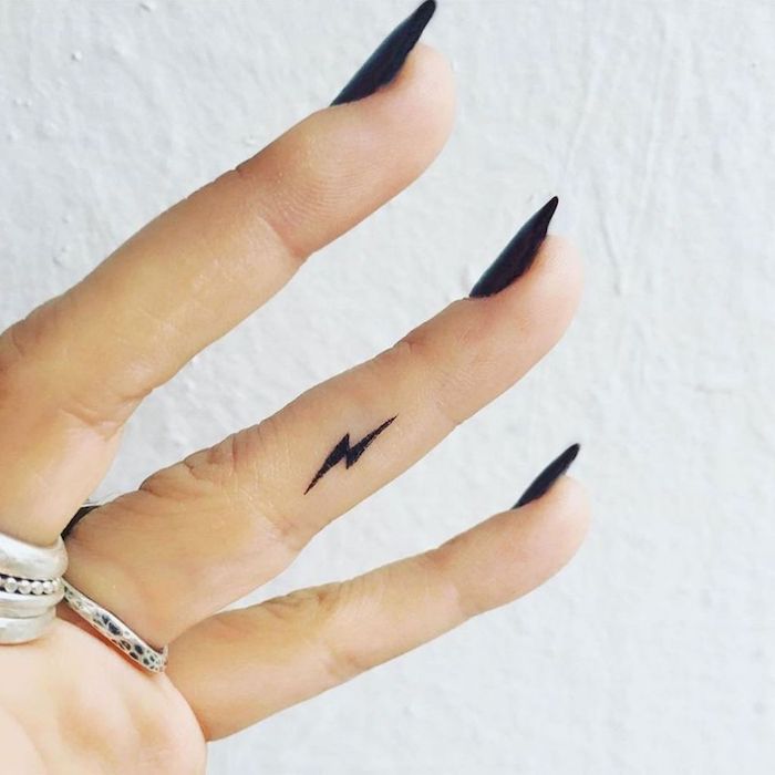 un petit éclair noir tatoué sur le côté du doigt annulaire, modèle de tattoo doigt discret et subtil