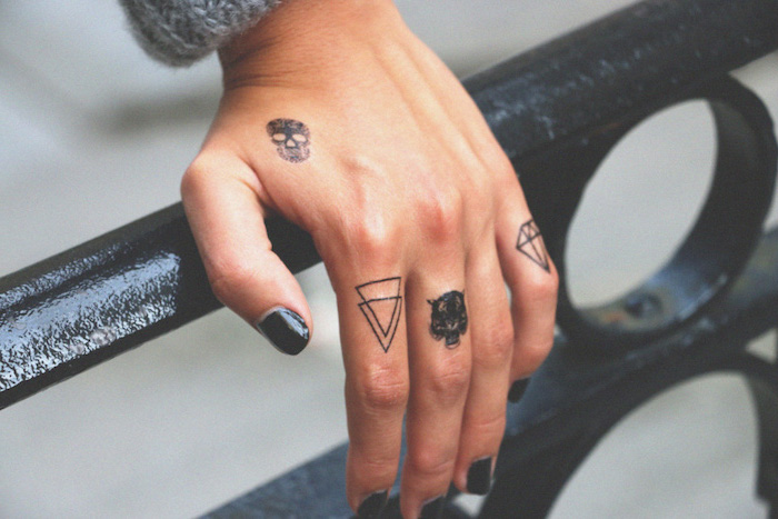 petits tatouages sur les doigts représentant une tête de mort, deux triangles, une tête de tigre et un mini-tatouage diamant