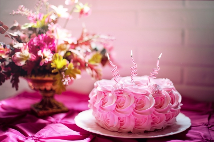 un simple gateau anniversaire fille au glaçage en roses avec trois bougies zig-zag posé à côté d'un joli bouquet de fleurs
