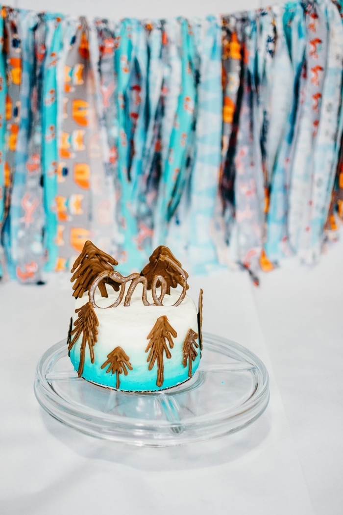 idée de gateau anniversaire garçon à réaliser soi-même, gâteau 1 an au glaçage blanc et bleu décoré avec des sapins en chocolat