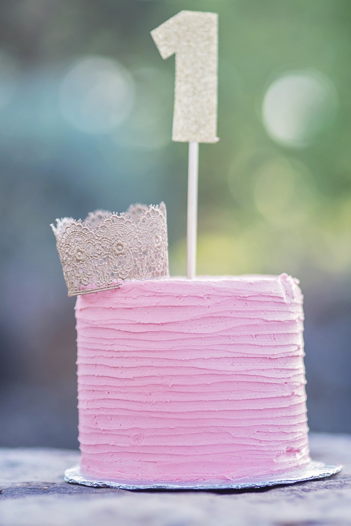 gâteau de premier anniversaire au glaçage rose décoré d'une petite couronne en dentelle et d'un topper chiffre pailleté, gateau anniversaire fille 1 an
