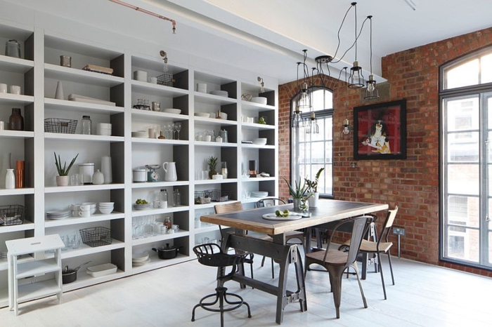 grande étagère grise, table rectangulaire en bois et métal, chaises design brut, mur en briques, fenêtres arquées