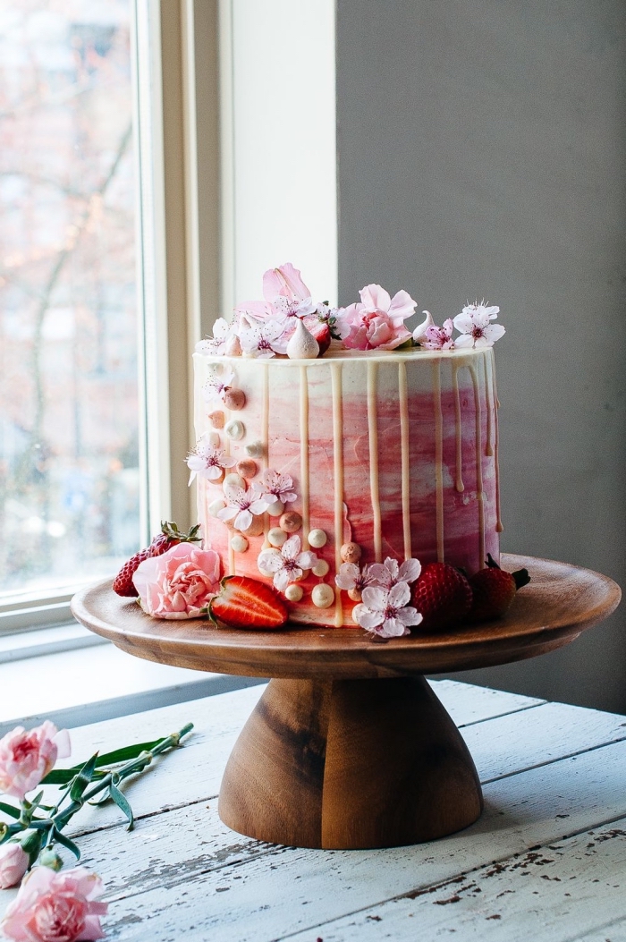 gateau anniversaire simple et beau au glaçage coulant de chocolat blanc avec une jolie décoration de fleurs de cerise et de meringues