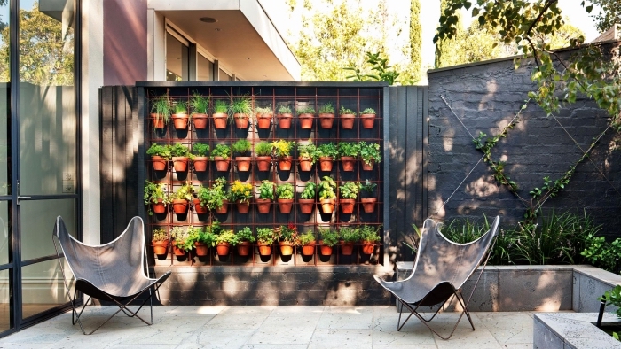 jardiniere haute avec des pots d'herbes aromatiques posés sur une grille métalliques, un adorable patio avec mur végétal 
