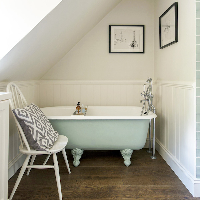 aménager une petite salle de bain avec sol de parquet marron, chaise blanche, baignoire vert clair, murs blancs et soubassement bois blanc