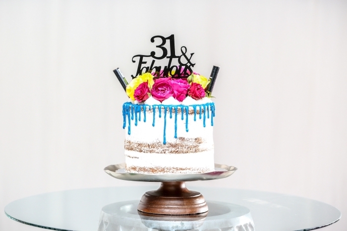 un gâteau d'anniversaire au glaçage coulant bleu décoré d'un cake topper personnalisé et de fleurs 