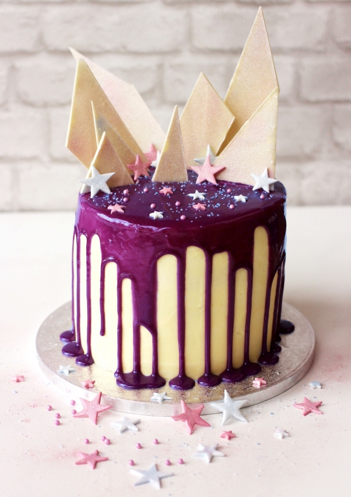 gateau anniversaire fille au glaçage coulant violet décoré d'étoiles en sucre et de copeaux de chocolat blanc 