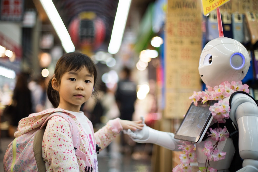 Belle fille voit un robot qui lui semble mignon, robot apprend à jouer à Jenga, robot avec guirlande de fleurs 