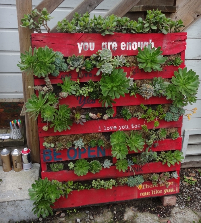 une jardiniere haute de plantes succulentes en palette recyclée repeinte en rouge avec citations inspirantes