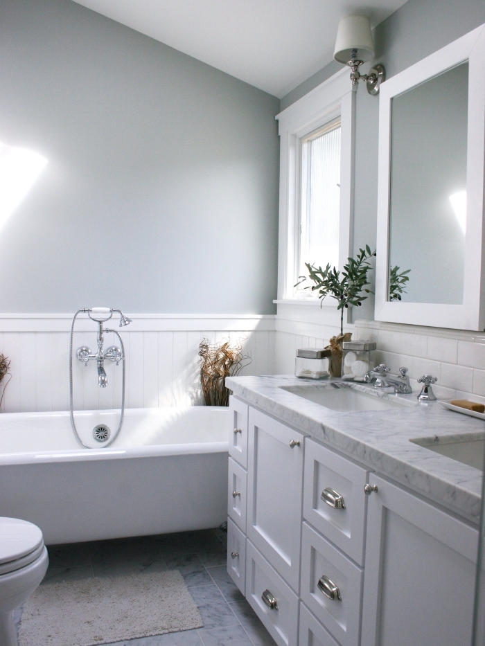 une salle de bains avec du lambris blanc en soubassement associé à une peinture murale gris perle et à du carrelage blanc métro