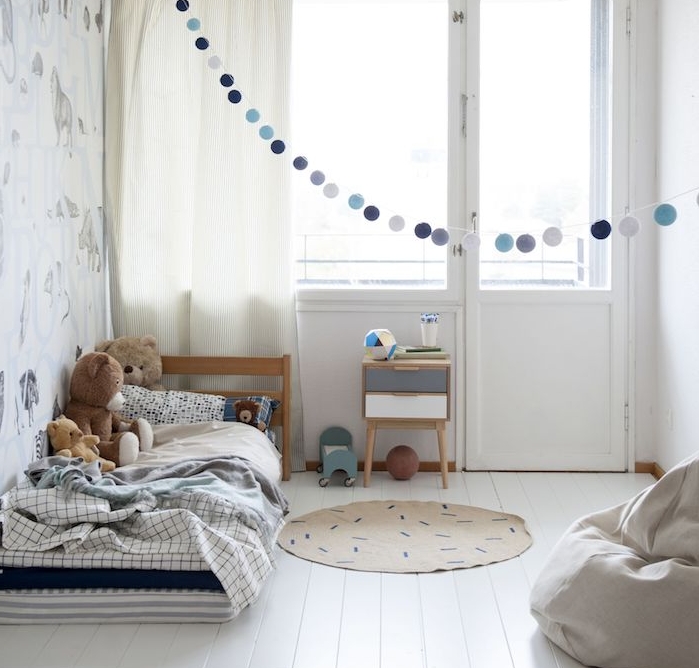 matelas ai sol couvert de linge de lit sur un parquet blanchi, murs blancs, guirlande de boules gris et bleu, barbaron gris