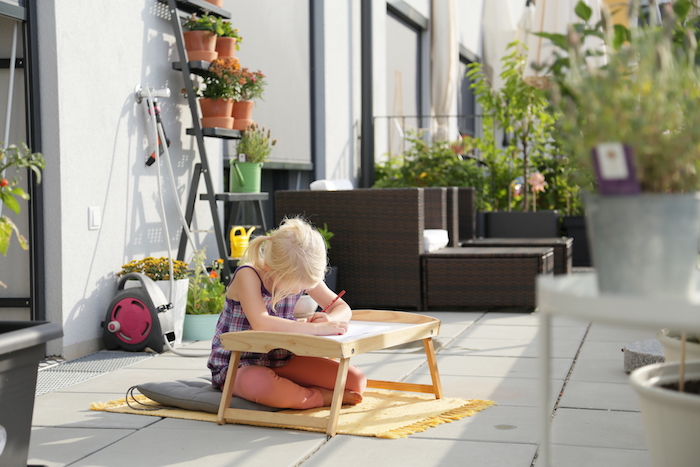 pédagogie montessori dans le jardin, table d'activité pour dessiner dans le jardin, coussin gris, tapis de jeu jaune