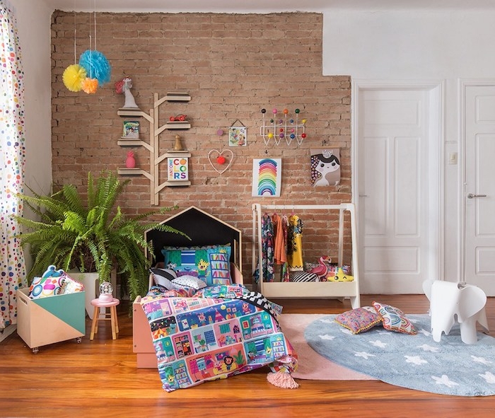 mur de briques decorative avec sol parquet bois, tapis rose et tapis rond, coffre à jouets à roulettes, dressing ouvert enfant