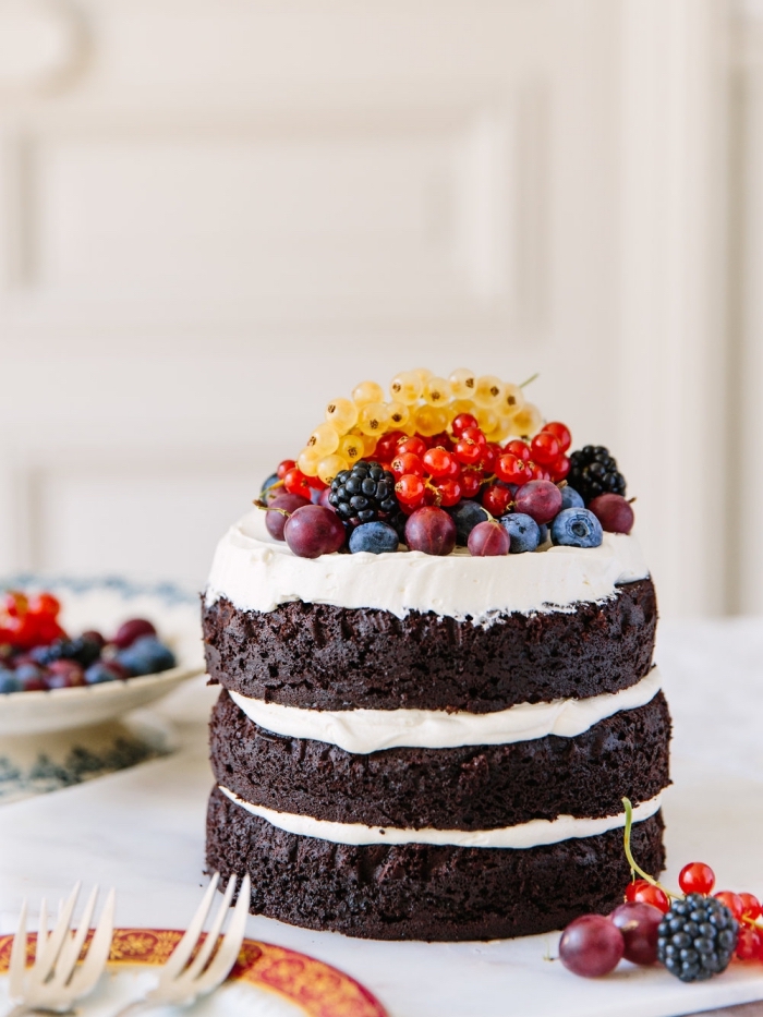 naked cake de trois génoises au chocolat fourré de glaçage blanc et décoré de fruits rouges et de groseilles