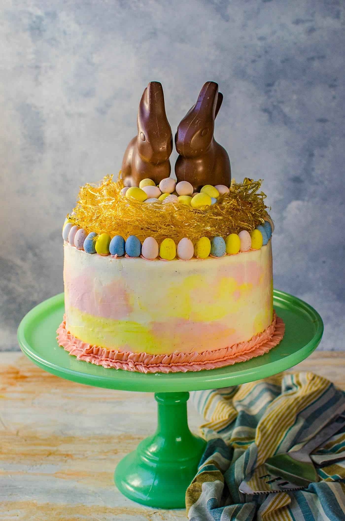 joli gâteau spécial pâques au glaçage dégradé en rose et jaune décoré d'un nid de paques en caramel et de deux lapins en chocolat