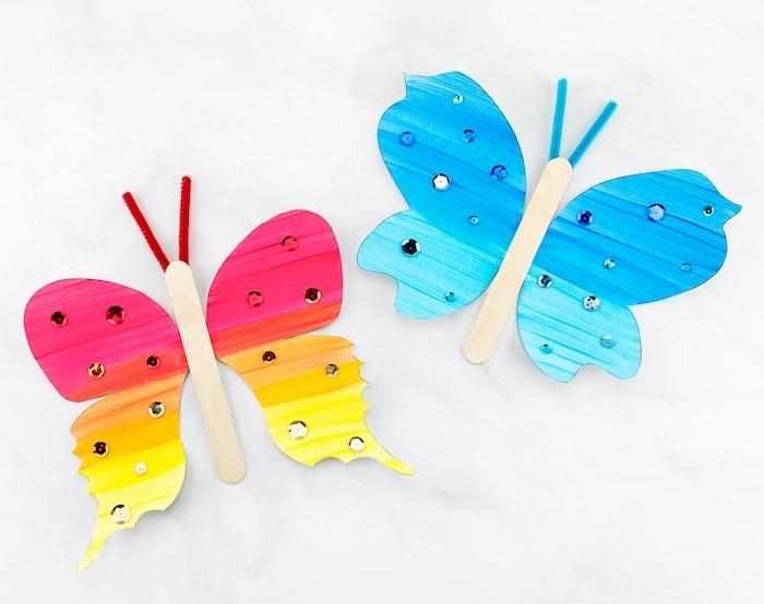 faire une papillon aux ailes de papier colorés et corps en batonent de glace décoré de strass, antennes en cure pipe