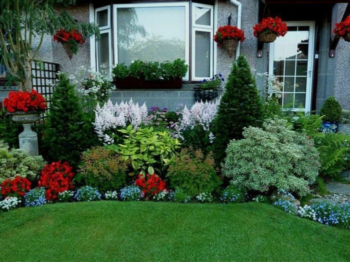 parterre devant maison avec fleurs variées et buies, pelouse verte, maison grise, jardinière à la fenêtre