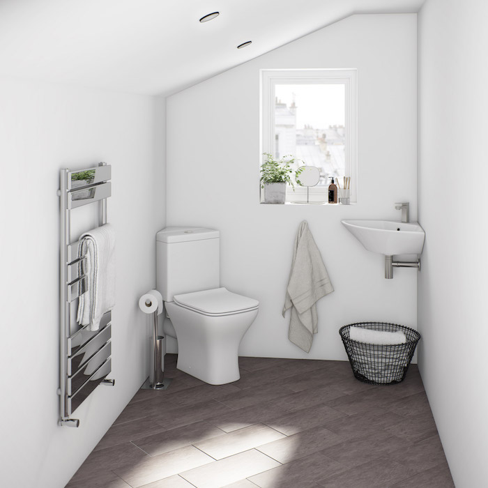 salle de bain avec sol gris et murs blancs, wc blanc et lavabo d angle blanc, plante sur un rebord fenêtre, porte serviette grise