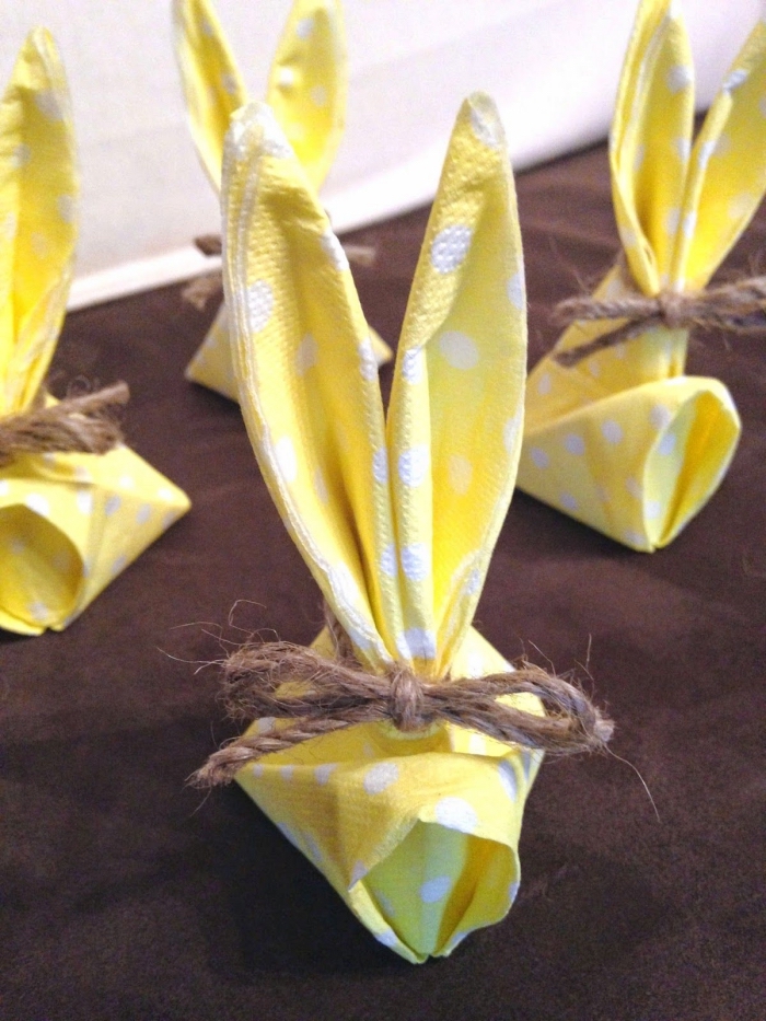 serviette en papier en forme de lapin pâques noué avec une ficelle en chanvre, petits lapins en papier jaune à pois blancs