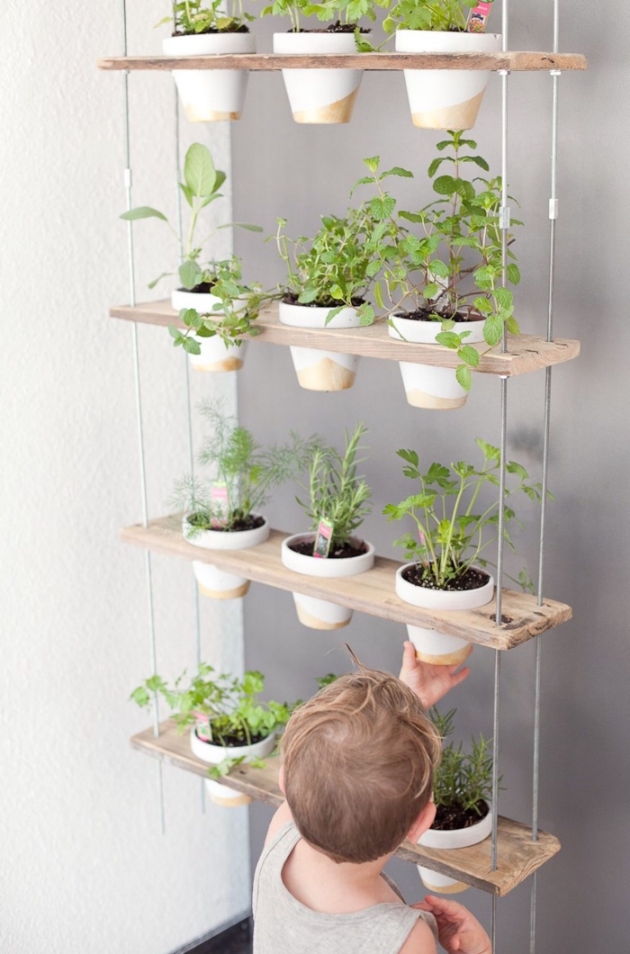 une suspension pour plantes en pots composée d'étagères en bois qui accueillent des pots d'herbes aromatiques, aménager un petit jardin en hauteur 