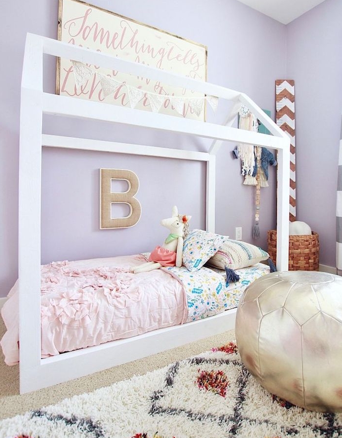 murs couleur violet et lit maisonnette blancs avec linge de lit coloré, tapis noir et blanc, pouf enfant, panier à jouets tressé