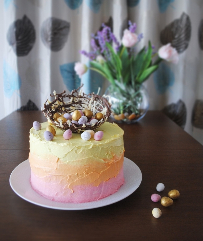 un layer cake nid de paques au glaçage dégradé de crème au beurre rose, orange et jaune avec un nid en chocolat noir et blanc