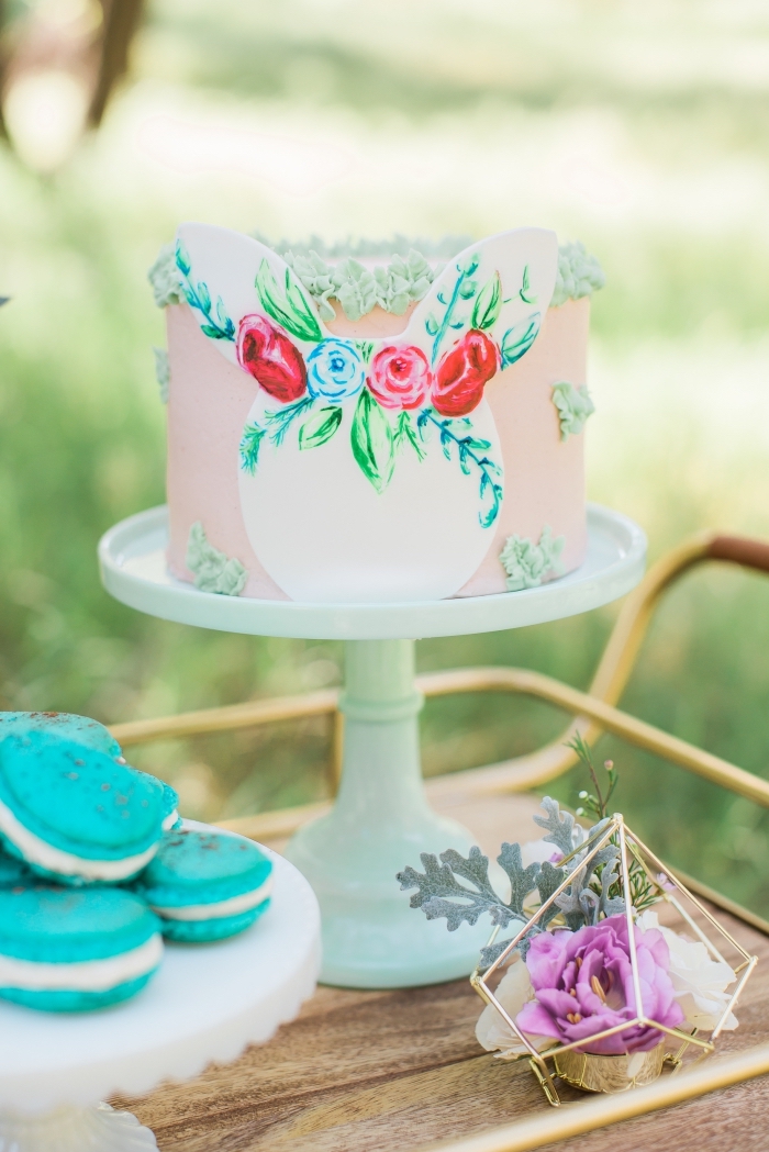 joli layer cake au glaçage lisse rose décoré de petites fleurs réalisées à la poche à douille et d'une tête de lapin en papier