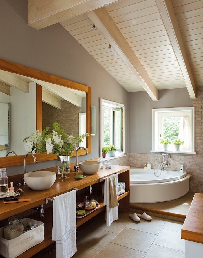 salle de bain bois et gris avec poutres apparentes blanches, carrelage sol beige, meuble salle de bain bois clair, vasque à poser blanc, miroir horizontal, baignoire d angle