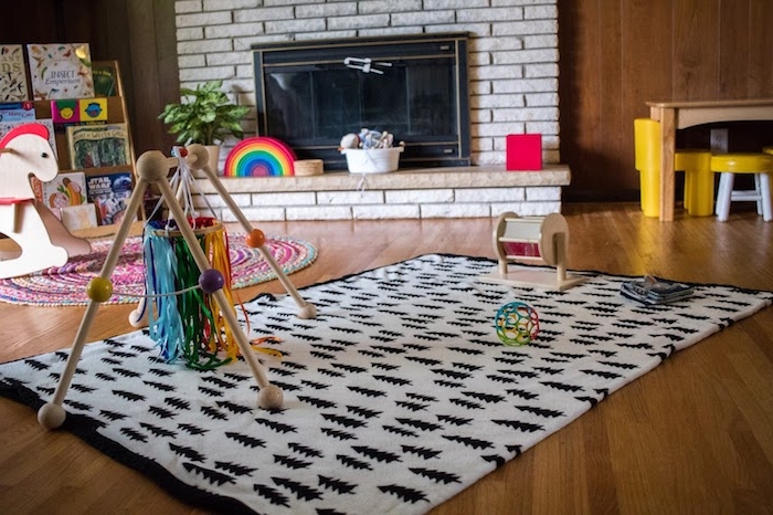 tapis d'éveil montessori avec un mobile montessori intéressant, tapis rond, cheval à bascule, cheminée salon