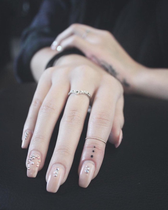 tatouage sur le doigt à l'esthétisme minimaliste composé de trois points réalisés sur l'index