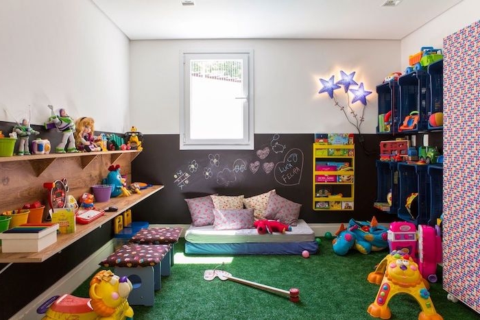 pan de mur soubassement en peinture ardoise avec dessins enfant, rangements étagère et cagettes en plastique, tapis imitation herbe, jouets enfant
