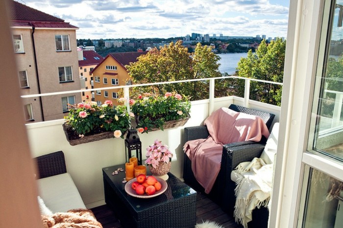 decoration balcon avec fauteuils et table basse noirs avec deco de plaids moelleux, deco de bacs à fleurs suspendus, sol bois marron usé