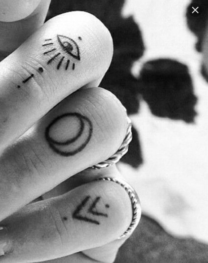 tatouage sur les doigts à motifs tribaux représentant un troisième oeil, des flèches et un cercle