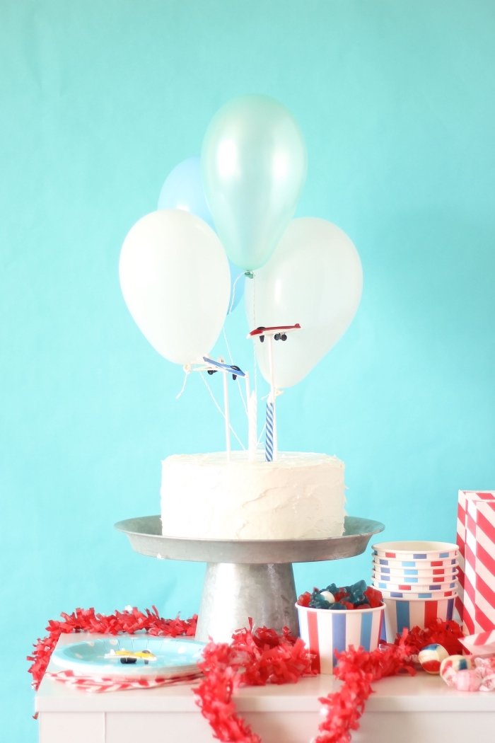 gâteau anniversaire garçon au glaçage blanc sur le thème avion décoré de petits ballons et de figurines avions