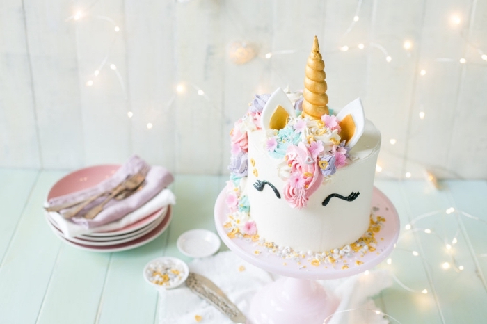 gâteau d'anniversaire en forme de tête de licorne au glaçage lisse blanc avec une crinière arc-en-ciel réalisée à la poche à douille, theme anniversaire licorne